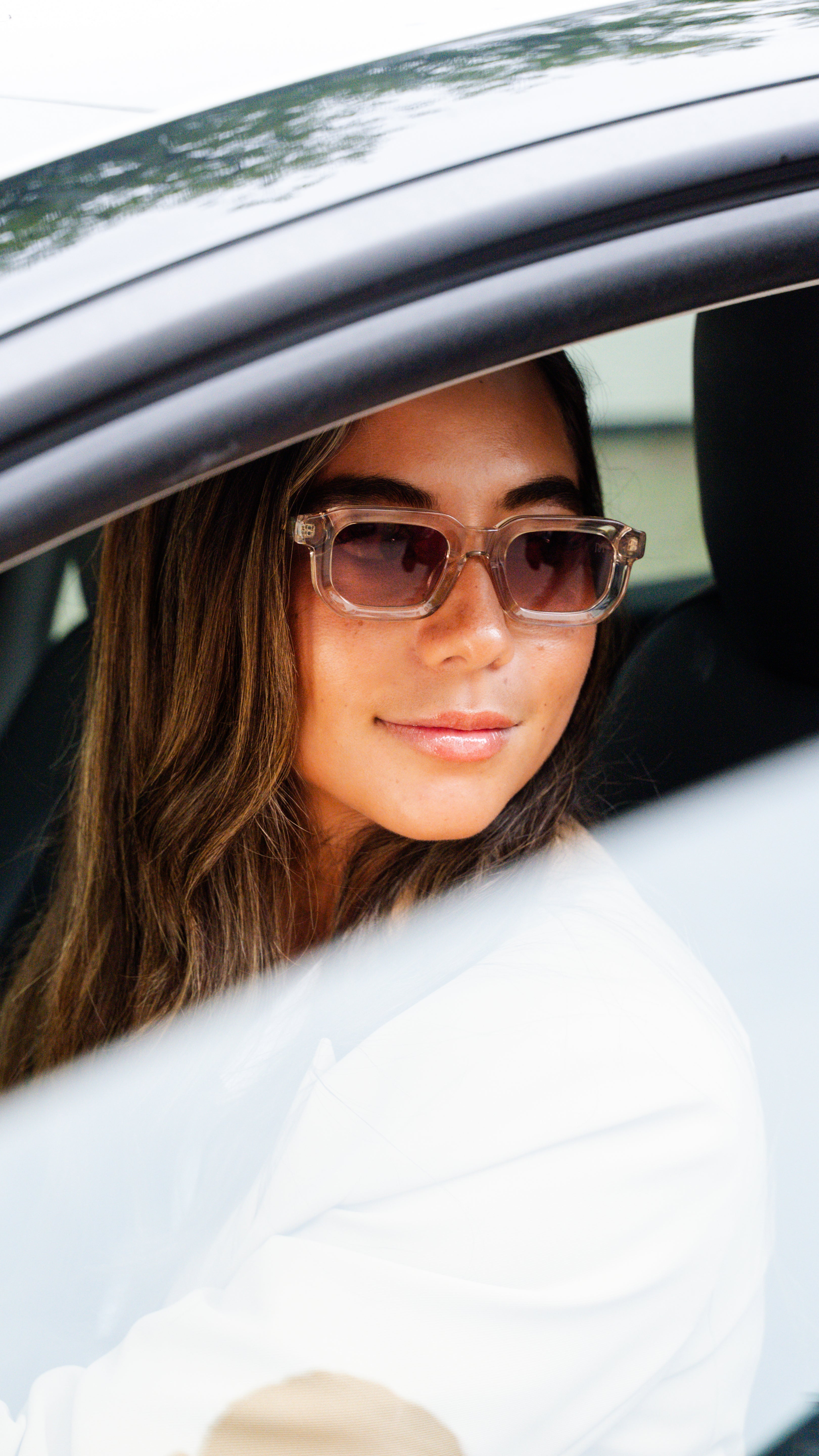 Vrouw draagt de UR3328 Royale zonnebril met nude acetaat frame, bruine gradient glazen, gouden details in de auto onderweg naar de stad.